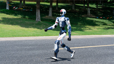 Unitree R1 Robot walking on a road with trees and grass in the background